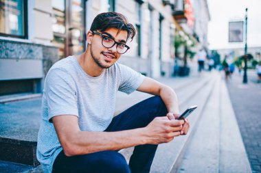 Sosyal ağlar üzerinde kentsel ayarı sokakta oturan ücretsiz 4 g internet bağlantısı kullanarak smartphone aygıt profili güncelleştirilirken kameraya gülümseyen göz gözlük başarılı öğrenci portresi