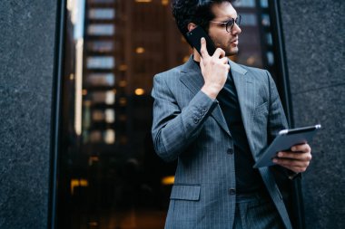 Kendine güvenen genç girişimci dijital tablet ise mali işler müdürü ile smartphone üzerinde konuşmak ve uzak ofis bina duran arıyorum elinde tutan formal giyim giymiş resim kırpılmış