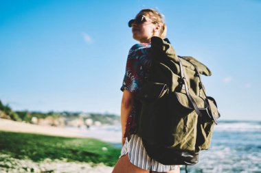 Tropikal Adası'nın doğal çevre yaz sondaj sırasında zevk güneş gözlüklü genç kadın turist arkasında şık seyahat sırt çantası seçici odak. Sırt çantası ile pozitif fiyatı