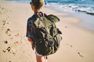 Kırpılan arkadan görünüm sırt çantası ile kadın turist tropik adada yaz gezisi sırasında yeni yerler keşfedin. Uzun yürüyüşe çıkan kimse yolculuk tutkusu kumlu kıyı şeridi boyunca sırt çantası ile. Sahil üzerinde yürüyen genç kadın