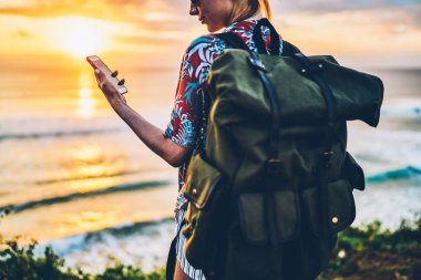 Haber sosyal ağ smartphone kablosuz internet kullanarak okuma yeşil sırt çantası taşıyan kadın Gezgin görünümünü geri. Hippi kız zevk yaz tatili görüntüsünü modern aygıtla kırpılmış