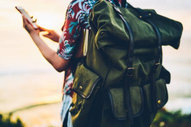Seçici odak rahat seyahat için yeşil sırt. Alacakaranlık anda deniz yakınında modern cihaz ile tatil zamanı geçirmek süre sırt çantası taşıyan kadın gezgin arkadan görünüm resim kırpılmış
