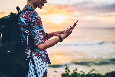 Okyanus manzara karşı ayakta yeniden oluştururken modern teknoloji kullanılarak yeşil sırt çantası ile mutlu kadın turist resim kırpılmış. Genç hippi kız açık havada twilight saat sırasında denizde rahatlatıcı