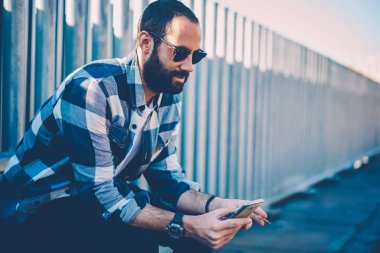 Sosyal ağ smartphone kablosuz Internet bağlantısı üzerinden içinde Genç sakallı adam okumak haber resim kırpılmış. İyi görünümlü erkek kişi bildirim sırasında yasaktır cep telefonu tarihinde kontrol güneş gözlüğü