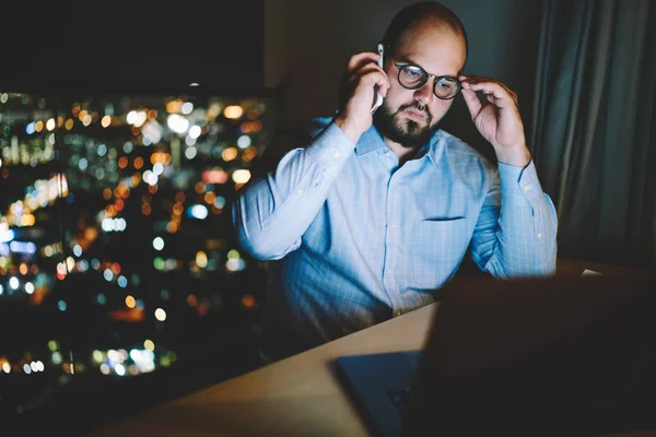 Contemplative businessman pondering during telephone conversation reading web site information on laptop computer,serious male freelancer talking on cellphone completing task before deadline