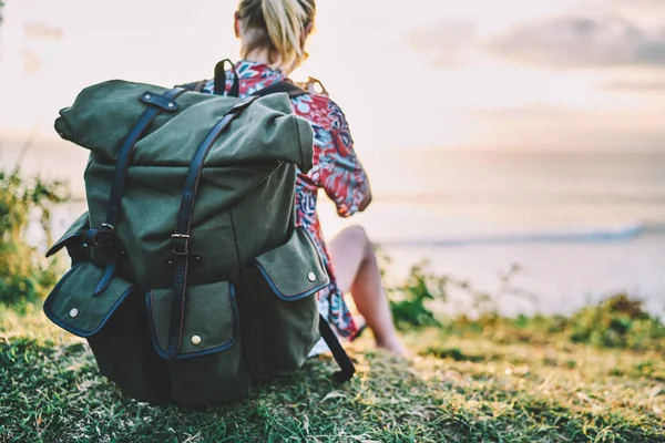 后面的女人旅行者穿着休闲的衣服放松在黄昏时间坐在一个大背包旁边的海洋 女性旅游者在近海时期再造的形象 — 图库照片