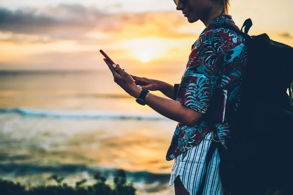 裁剪形象的积极时髦的女孩穿着休闲服装享受夏季度假的海洋景观 带背包的年轻女性游客通过电话向朋友发送信息 — 图库照片