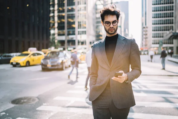 Confident proud ceo in suit checking notification from banking app on smartphone strolling on Manhattan,handsome prosperous businessman dressed in fashion formal apparel reading message on cellula