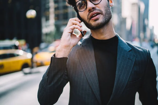 Cropped image of confident male boss in elegant suit using business tariff for making mobile call in roaming, handsome man in formal apparel having telephone conversation walking on Manhatta