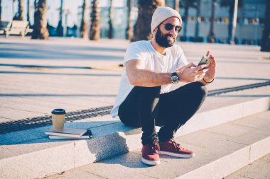 Siyah güneş Smartphone cep telefonu ile iyi haberlerle bildirimi alındı gelen mutlu hipster adam sakallı. Neşeli erkek blogger cep açık havada merdivenlerde oturan internet üzerinden yeni yayında yayımlama
