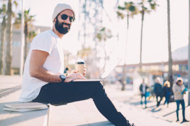 Kurs, 4 g kullanarak dizüstü bilgisayar üzerinde çalışırken kameraya gülümseyen güneş gözlüğü styish sakallı öğrenci portresi kahve molası sırasında kentsel ortamda merdivenlerde oturan internet