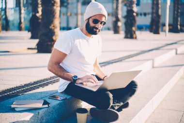 Web sitesi Internet modern dizüstü aygıta bağlı 4 g üzerinden online paytment yapma güneş gözlüğü erkekte Yung sakallı. Şık öğrenci bilgisayar açık havada merdivenlerde dinlenme üzerinde e-posta kontrol