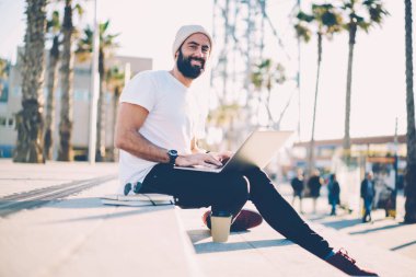 Neşeli portre kameraya gülümseyen dizüstü bilgisayar kullanarak Internet Web sitesinde web grafik tasarımcı çalışma sakallı. Mutlu öğrenci şehir merdivenlerde dinlenme netbook sohbet keyfini serbest zaman