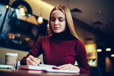 Kurs proje için hazırlanıyor ve bazı kapalı oturma sırasında notating yapım genç durulması akıllı kız öğrenci. Kafede Not defteri bilgileri kaydetmek çekici dalgın hippi kız