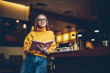 Genç çekici yaratıcı kadın blogger kişisel web sitesinde başarılı yayın hakkında trendy elbise rüya giyinmiş. Yetenekli sarışın öğrenci ders çalışma için fikirler kaydederken durulması