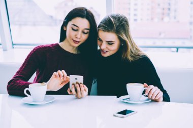Pozitif güzel arkadaşlar giyinmiş trendy giyim Web sitesinde 4 g için bağlı hücresel komik Haberler okuma Internet. Muhteşem kadın modern araç ve lezzetli kahve ile boş vakit