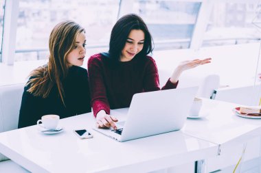 Şaşırmış gibi esmer ve sarışın öğrenciler dizüstü bilgisayar şık restoranda oturan şok video izlerken. İki arkadaşları kahvehane iç oturan internet sitelerinde haber okuma