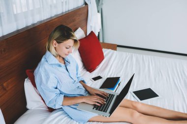 Genç kadın yatakta, kadın blogger otel odasından uzaktan web sayfası uğraşıyor tatil hakkında bilgi güncelleme yalan sırasında serbest üzerinde çalışan dizüstü bilgisayarda metin yayın yazma