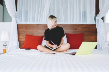 Zeki kız öğrencinin not defteri bilgileri web sayfasından dizüstü bilgisayar vasıl ev eğitim genç kız yatağa Notlar eğitim webinar izlerken netbook ile oturup ödev yazma