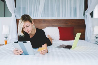 Dalgın kız öğrenci kredi kartı için çevrimiçi eğitim webinar web store tablet rahat ev alışveriş ve app içinde ödeme yapma tarama genç kadın yatakta, yatarken taşınabilir pc üzerinden ödeme ile