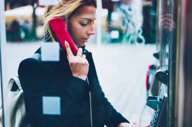 Düşünceli kadın turist yapma çağrısında sokak şeffaf kabine genel telefon çağrısı ile düşük fiyatlar yurtdışında seyahat sırasında paralar ile işletilen kullanan genç kadın ayakta üzerinde ödemeli telefon