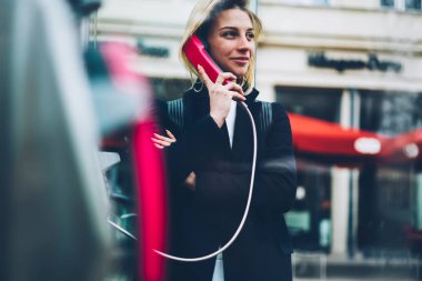 Bağlantı yolu ile sabit telefon kulübesinden seyahat şehir merkezinde söz şehir sokak, pozitif genç kadının üzerinde uluslararası konuşma duran için gülümseyen sarışın kadın turist memnun