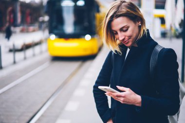 Gülümseyen genç kadın tablo şehir trafik online smartphone kullanarak web sayfası denetimi, app yolu ile cellphone tramvay için bekleyen elektrik taşıma için ödeme için olumlu hippi kız memnun