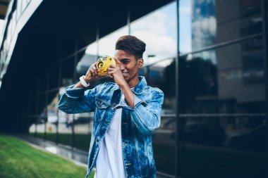Yetenekli hindu genç adam modern fotoğraf makinesi odaklama ve boş zamanlarında en sevdiği hobi zevk serin fotoğraf yapma şık denim giyim giymiş. -Konuşan resimler açık havada yaratıcı erkek öğrenci