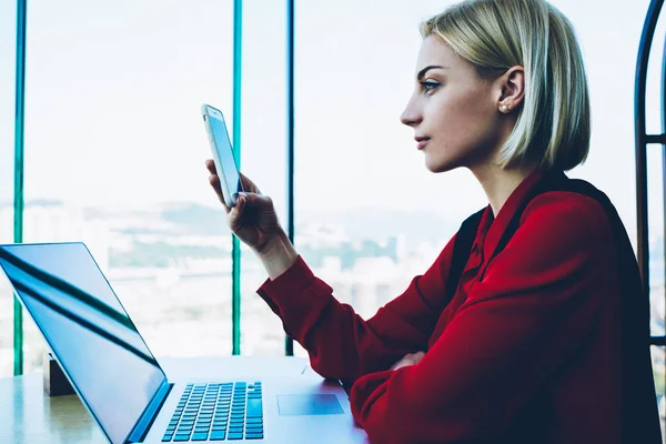 Professional administrative manager checking messages on cellular sitting at working place in office, businesswoman browsing website on telephone checking information for contact service operator