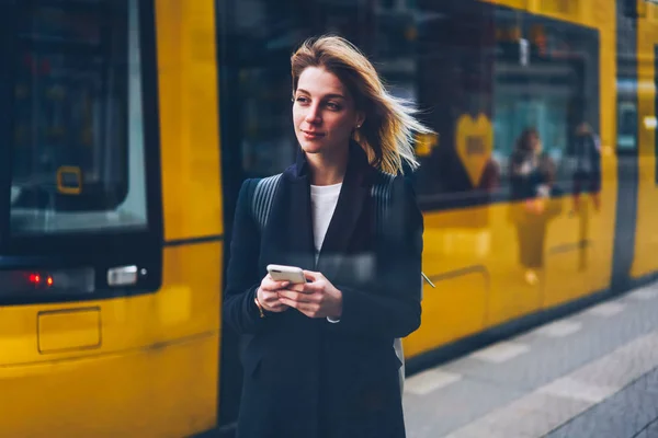 市バスのオンライン情報を取得する携帯電話アプリケーションを使用して停止の輸送を待っている女性旅行者の交通インフラのオンライン テーブルをチェックするスマート フォンを保持している若い女性 — ストック写真