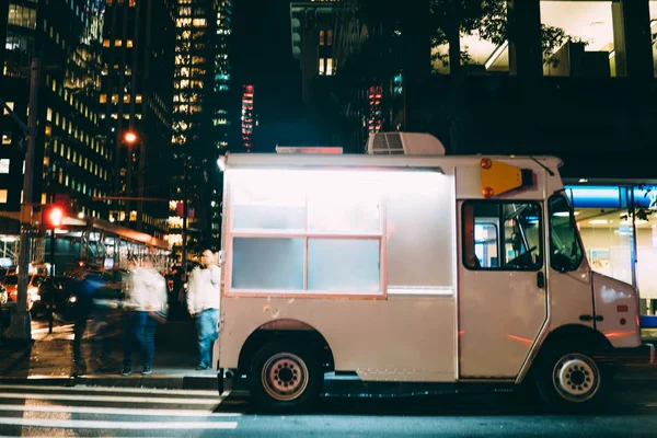 White food truck parked on city street near buildings using for retail business startup, Van automobile with mock up copy space area for brand name selling ice cream parked in urban setting at night