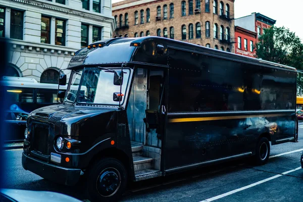 Black van automobile of logistic company driving on roads in megapolis delivering goods, postal truck body with copy space area for delivery service name or logo and advertising information