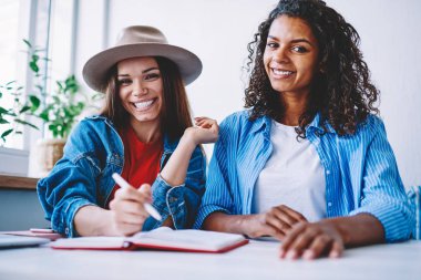 Neşeli genç kadın tasarımcılar birlikte modaya uygun kıyafeti planlama ve denetim listesi yapma kameraya bakarak hipster kızlar samimi bir atmosferde, ortak proje üzerinde taslak yapma portresi