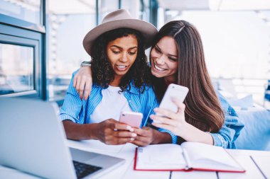 Komik arkadaşlar trendy kıyafeti cep telefonlarıyla birlikte dinlenme sırasında ortak fotoğraf gönderme dosyaları eşitleme, Smartphone cep telefonu ile güncelleştirme resmi hipster kızlar bloglama sosyal ağlar