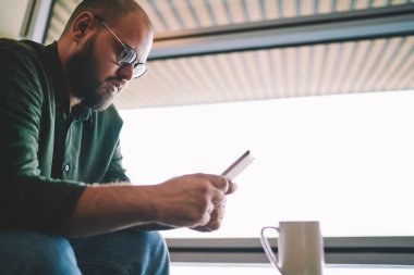 Öğretici Smartphone kablosuz 4 g internet bağlantısı üzerinden yükleme hareket eden app için izlerken Eyewear dalgın genç adam. Sakallı blogger online folowers calluler kafede üzerinde sohbet