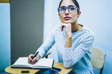 Düşünceli kadın Eyewear kolej sınıf, Masa başında oturan ev ödevi görevi öğrenme üzerinde durulması dalgın kız öğrenci test yazarken bilgi hatırlatarak Vizyon Düzeltme