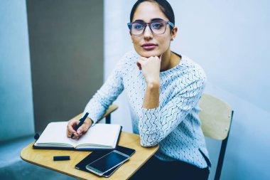 Dil Okulu için öğrenim Not defteri ile masa başında oturan dalgın genç kadın geliştirmek becerileri ve bilgi, kız öğrencinin ders notları öğrenme sırasında sınıfta yapmak için fikir düşünüyorum