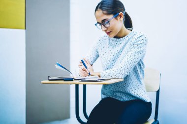 Ciddi akıllı genç kadın ile not etmek, zeki kız öğrencinin notları ve araştırmaları sırasında otodidakt bilgi yapma sınıfta öğrenme masa başında oturan üniversitede testi test yazma