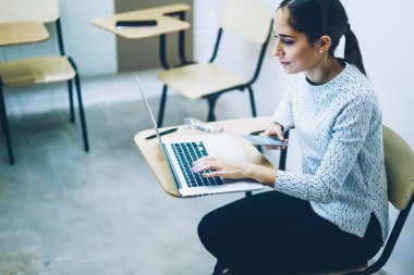 Dalgın kız öğrencinin Üniversite sınıf, Genç kadın online eğitim kursları eğitim sırasında bilgi ve becerilerini geliştirmek netbook üzerinde izlerken oturup öğrenmek için dizüstü bilgisayar kullanan