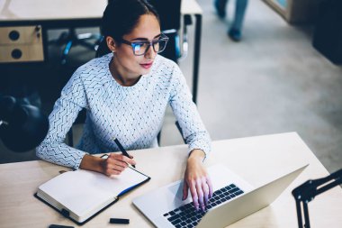 Vasıflı iş kadın giyim gözlük vizyon koruma çalışma işlemi, profesyonel kadın Yöneticisi not defterinde planlama netbook üzerinde bilgi arama sırasında dizüstü bilgisayar monitörü seyir için
