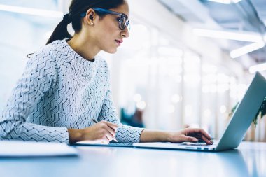Profesyonel yönetim yönetmek içinde gözlükler gözleri koruma kontrol içeriğini şirket web sitesinde dizüstü bilgisayar, ciddi kadın Sekreter ofiste çalışan netbook üzerinde rezervasyon yapmak için
