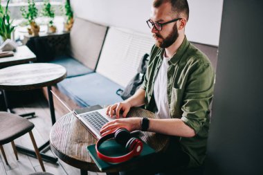 Çatı katı iç ve uzaktan çalışma ile kafede oturan gözlük ciddi yetenekli beyaz programcı, genç düşünceli laptop ve fikirler için kurs metin yazarak izlerken webinar adam.