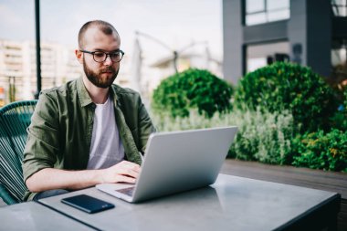 Genç hipster adam gözlük at açık havada Sokak kafede oturan vizyon koruma için bağlantılı kablosuz internet ve izlemek video online akıllı adam yeni modern dizüstü bilgisayar kullanarak çevrimiçi öğrenme