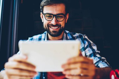 Pozitif sakallı genç adam gözlük vizyon düzeltme 4 g ile modern tablet Web sitesinde canlı akışı izlemek için internet. Touch pad aygıt üzerindeki iletim online zevk neşeli erkek blogger