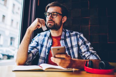 Kartvizit smartphone ile kafede oturan çalışma önerisi üzerine düşünme elinde düşünceli sakallı hippi herif. 4 g üzerinden para işlem üzerinde durulması dalgın genç adam cep internet