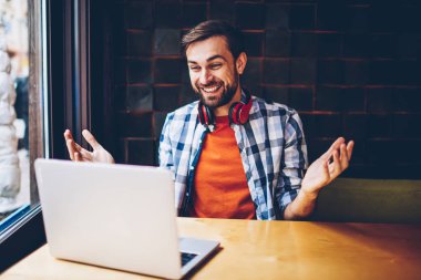 Mutlu sakallı hippi blogger modern dizüstü bilgisayarda görüntülü görüşme yoluyla arkadaşlarınızla iletişim kurmak için kablosuz 4 g bağlı internet. Komik eğitsel bir netbook izlerken boyun kulaklık ile pozitif genç adam