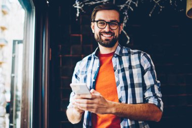Mutlu portre alan coworking içinde smartphone aygıt ayakta kısa mesaj yazarken kameraya gülümseyen genç adam sakallı. Pozitif hipster adam Online sosyal ağlar üzerinde telefon sohbet