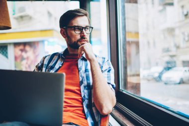 Düşünceli sakallı grafik tasarımcı düşünme üzerinde Web sitesi geliştirme ve modern dizüstü cihaz alan coworking içinde ücretsiz 4 g internet bağlantısı kullanarak, serbest çalışma pencereden dışarı seyir için fikirler