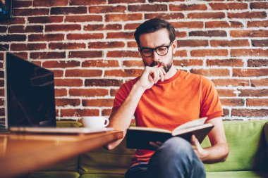Akıllı hipster öğrenci ders kitabı hazırlama semineri için bilgilerin öğrenme konsantre. Coworking modern netbook ile masada oturan görev çalışmaya düşünme dalgın genç adam