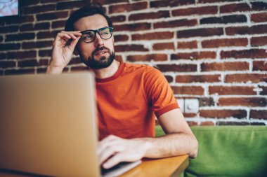 Düşünceli sakallı genç adam netbook, serbest çalışma bağlı 4 g için Internet süre uzağa bakıyor ve kendi yaratıcı fikirler geliştirmek düşünüyorum. Düşünceli blogger yayın üzerinde durulması